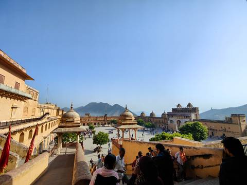 Tourists exploring a large courtyard of an ancient fort with hills in the background.