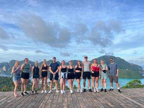 Group of people posing with a scenic mountain and ocean backdrop.