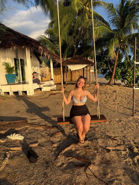 Person enjoying a swing on a sandy beach with a sunset backdrop.
