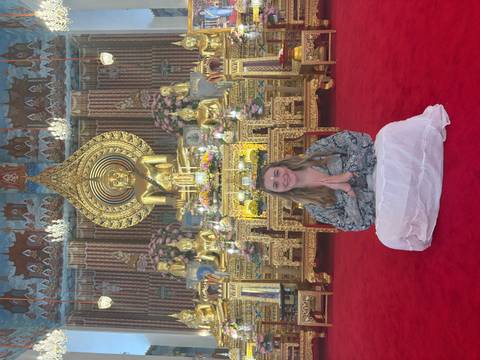 Person meditating in front of a Buddha statue inside a temple.
