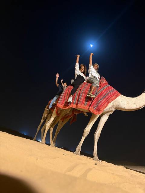       People riding camels at night in the desert.
  