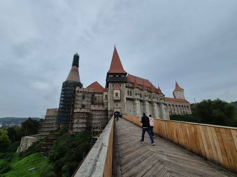       Corvin Castle with tourists on the bridge approach.
  