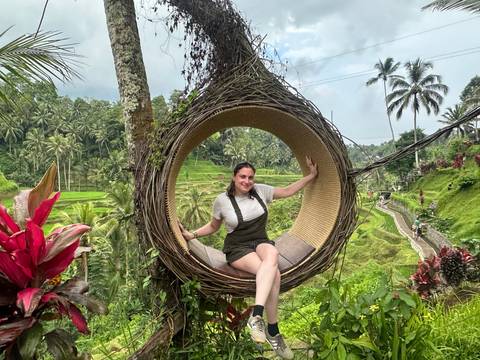 Person sitting inside a large decorative swing with rice terraces in the background.