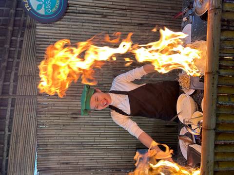 Smiling cook with a large flame in a kitchen setting.