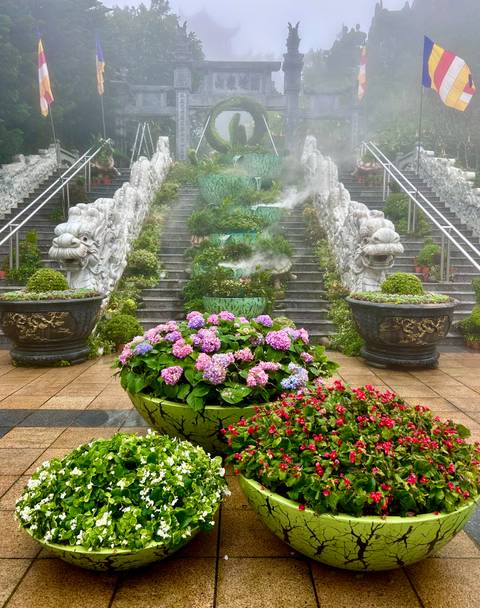       Decorated stone staircase and vibrant flowers on a misty day.
  