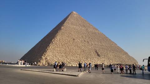 The Great Pyramid of Giza with tourists walking around it under a clear sky.