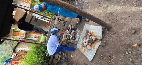       People preparing a meal outdoors with stones and a tarp.
  