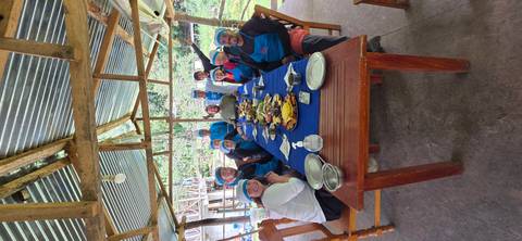      Group of people having a meal at a long table under a shelter.
  