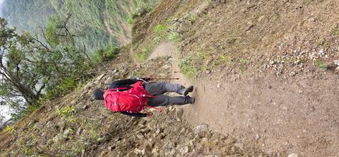       Person walking on a narrow trail along a steep hillside.
  