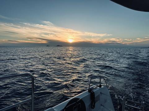       Ocean view at sunset with a boat railing in the foreground.
  