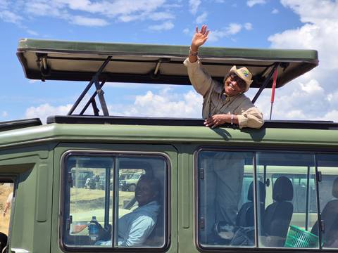 Person waving from a safari vehicle with an open roof.
