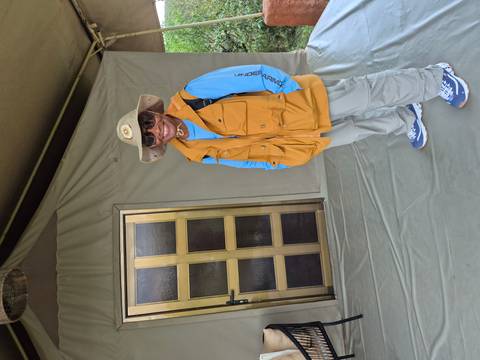 Woman posing in front of a safari tent wearing a hat and sunglasses.