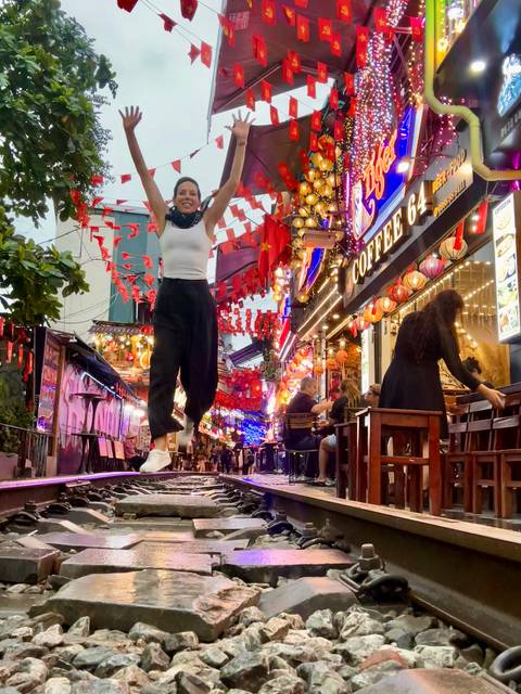 Person jumping joyfully on a street with vibrant decorations and lights.
