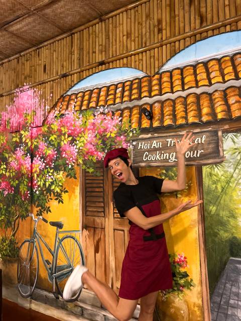 Person posing enthusiastically in front of a colorful mural with flowers.