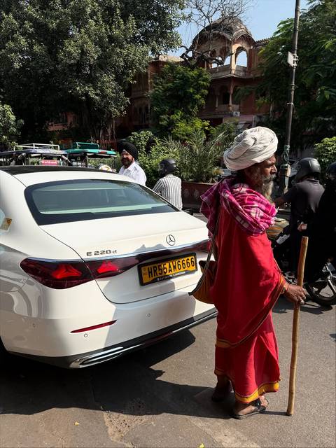 A man in traditional attire walking in front of a car on a busy street.