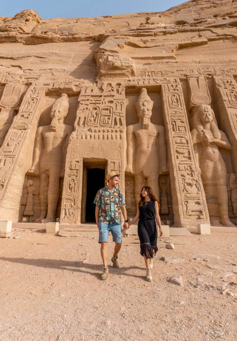 A couple holding hands in front of ancient Egyptian carved statues.