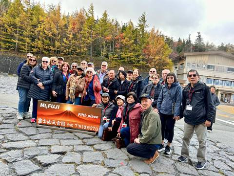       Group of people posing with a sign in front of a scenic mountain view.
  