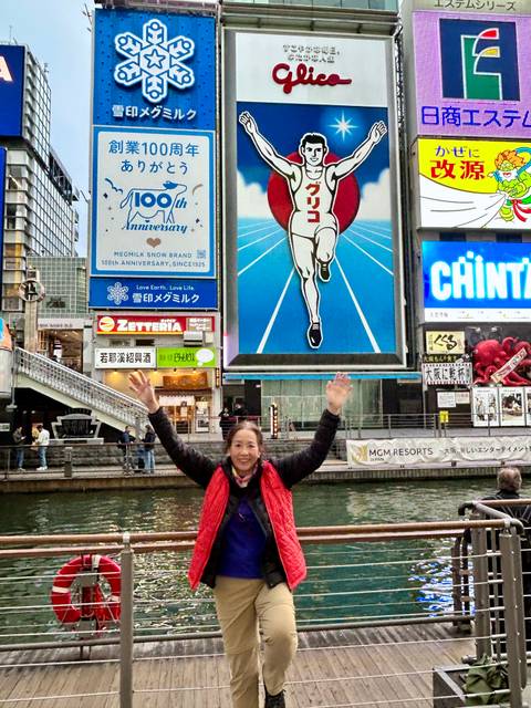       Tourist posing with famous running man billboard in a busy city area.
  