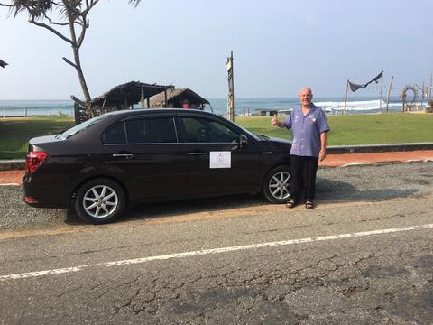 Man standing next to a parked car on a seaside road.