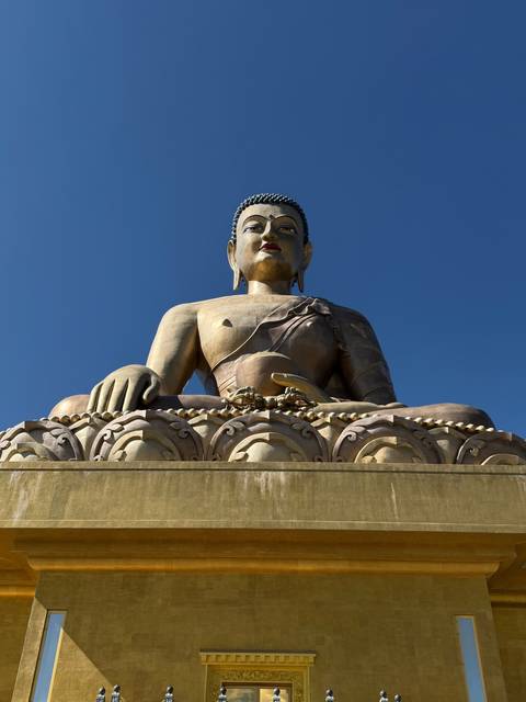       A large Buddha statue against a clear blue sky.
  