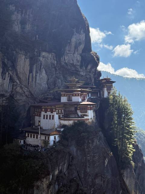       A monastery built into a cliffside with a forested background.
  