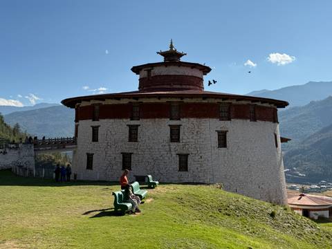       A round fortress with a red roof and scenic mountain views.
  