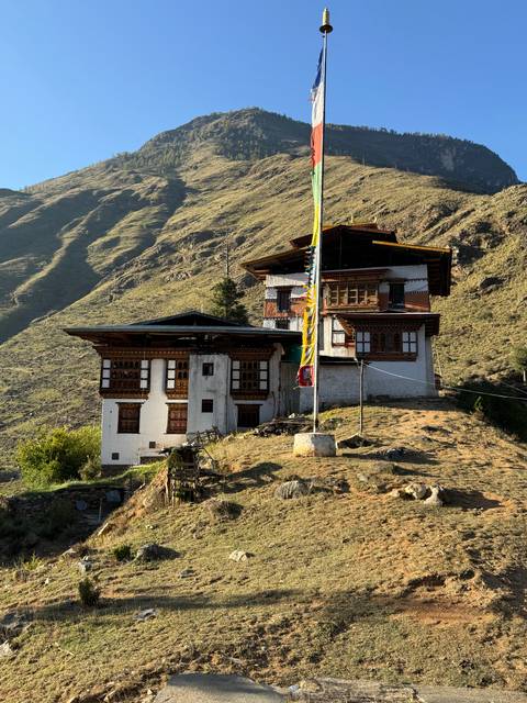       A traditional house on a hillside with flags and sunlit scenery.
  