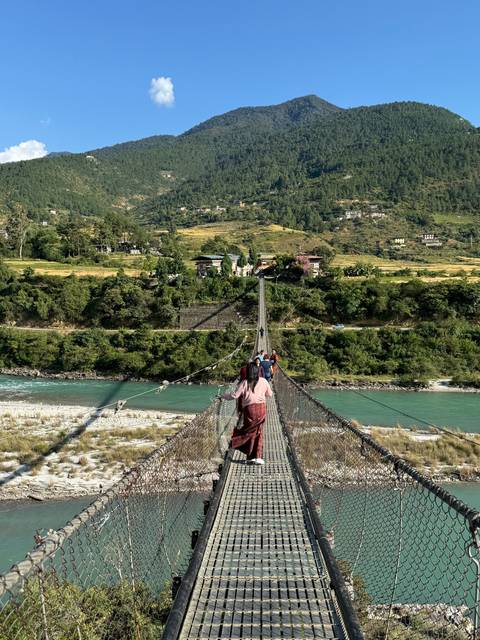       People walking on a suspension bridge with a scenic valley background.
  