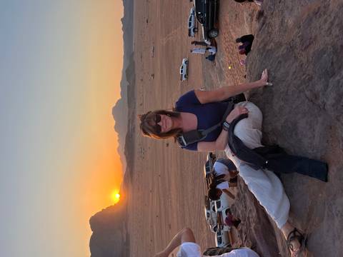 Person seated on rock with desert landscape and sunset.