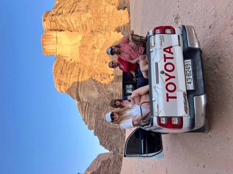 Group of tourists sitting in the back of a pickup truck in a desert.