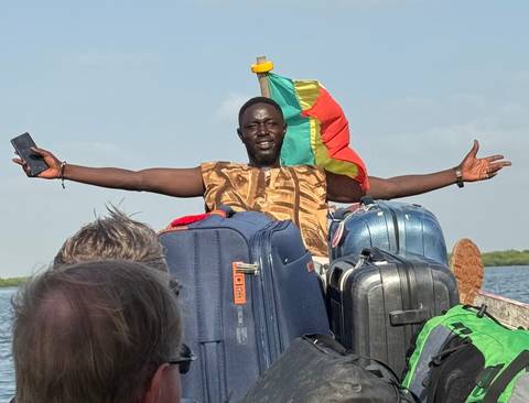 Person with spread arms on a boat surrounded by luggage and a flag.