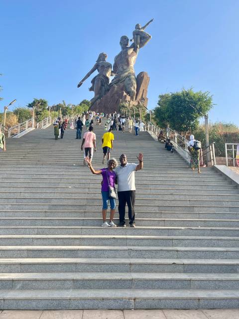 Two people posing at the base of a wide staircase on a sunny day.