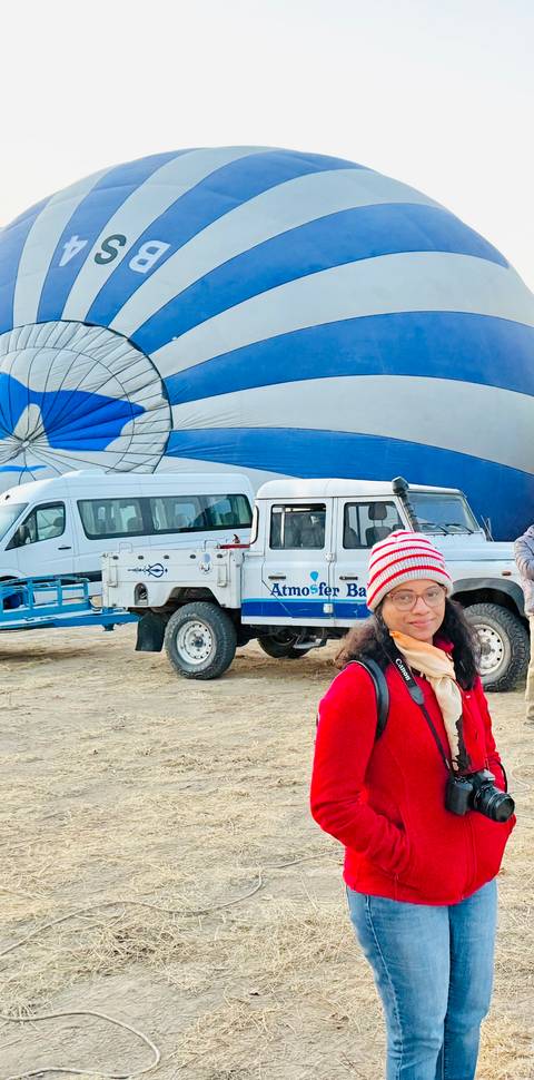       Person standing in front of a hot air balloon and vehicles.
  