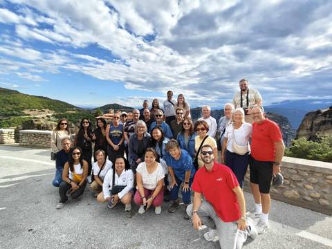 A large group of people posing together with a scenic view of mountains and a cloudy sky.