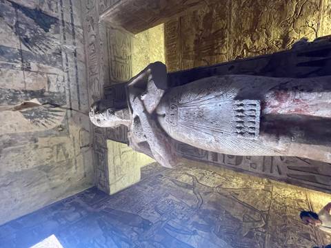 Pharaoh statue inside an ancient temple with hieroglyphs.