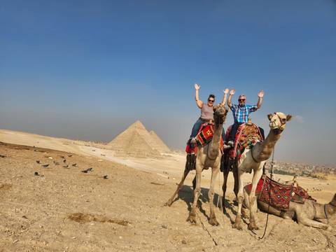 People riding camels in front of pyramids.