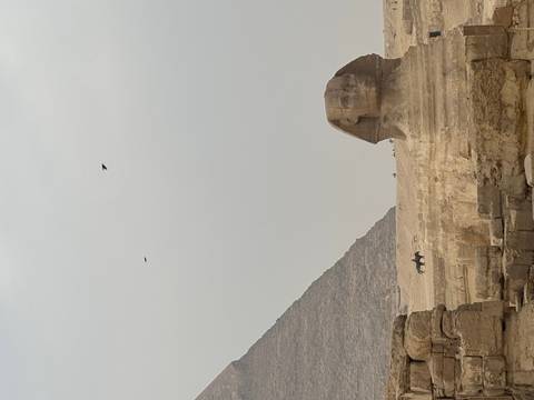       View of the Sphinx and a pyramid under a cloudy sky.
  
