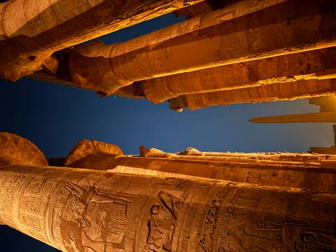 View of ancient columns and an obelisk at night.