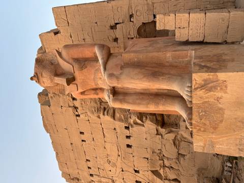 Statue of an ancient Egyptian pharaoh seated, with hieroglyphs on the wall behind it.