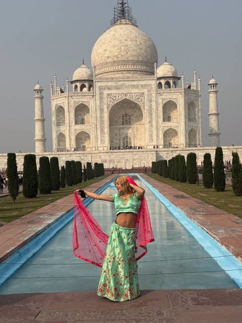 Woman in traditional dress posing with the Taj Mahal in the background.