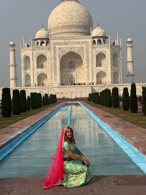 Woman posing with the Taj Mahal, standing by the reflecting pool.