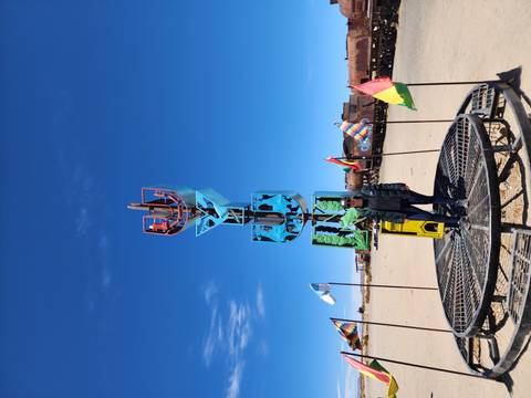 Person standing among flags beside a metal sculpture in the desert.