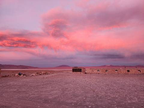 Dramatic pink clouds at sunset over a desert landscape with a building.
