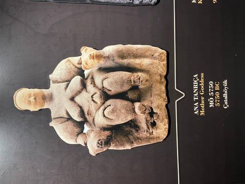 Statue of a seated figure with animals on a black background with text.