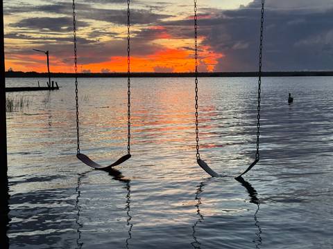 Two swings over water with a vibrant sunset sky.