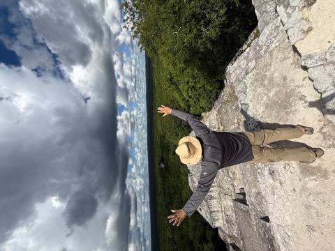 Person standing on a rock ledge with arms raised.
