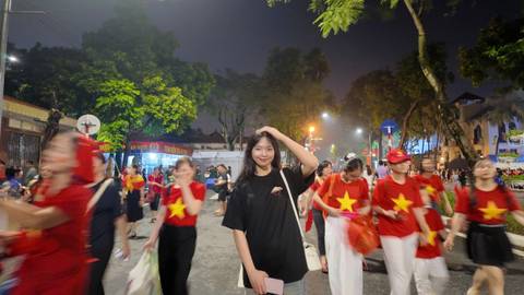       A young woman standing in a busy street at night with blurred motion around her.
  