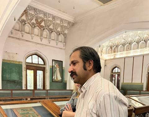       Interior of a historical building with a man in focus, showing ornate designs.
  