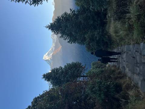 Two people hiking on a mountain path with a snowcapped peak in the background.