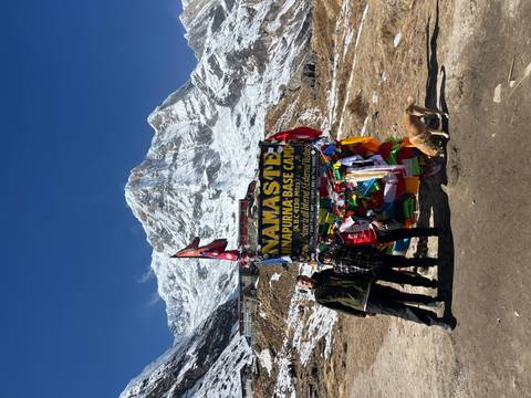 Group of people at Annapurna Base Camp with colorful flags and a mountain backdrop.
